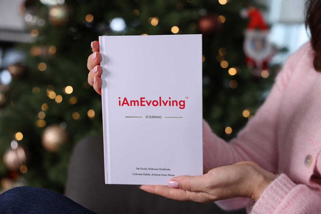 A person holding a minimal hardcover journal in a softly lit indoor setting, with warm, out-of-focus lights in the background. The centered composition and neutral tones create a calm, intimate atmosphere. The image represents reflection, mindfulness, and intentional living, capturing a quiet moment of pause and focus. Suitable for themes related to journaling, personal growth, self-reflection, lifestyle, and everyday moments of thoughtful simplicity.