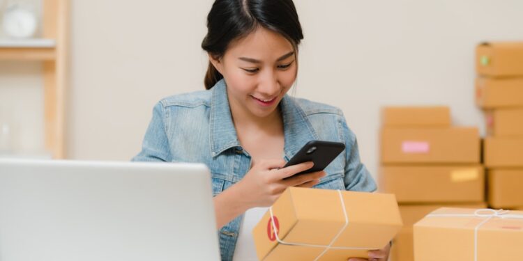 Beautiful smart Asian young entrepreneur business woman owner of SME checking product on stock scan qr code working at home. Small business owner at home office concept.