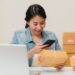 Beautiful smart Asian young entrepreneur business woman owner of SME checking product on stock scan qr code working at home. Small business owner at home office concept.