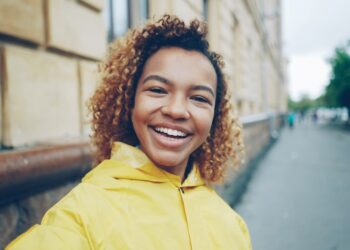 Point of view shot of cheerful young woman blogger looking at camera, talking recording video for her online vlog in the internet standing outdoors in the street.