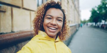 Point of view shot of cheerful young woman blogger looking at camera, talking recording video for her online vlog in the internet standing outdoors in the street.