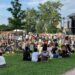 A concert crowd seating on the grass at an open air classical music concert