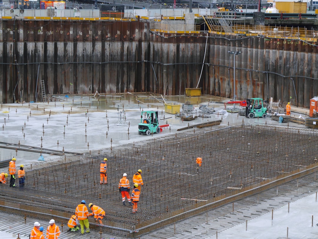 Construction site with workers on the concrete bottom, fixing the steel wire construction ground of the excavation site;. Then the concrete can be poured. This becomes an underground parking place for circa 8000 bicycles in front of Central Station, Amsterdam. The rusty pile sheeting wall is necessary to keep the construction pite safe and dry, because of the wet soggy bottom of Amsterdam city. Free urban photo of Amsterdam constructions - Dutch city photography of work by Fons Heijnsbroek, Netherlands.