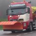 Strooiwagen met oranje sneeuwschuiver op een winterse weg